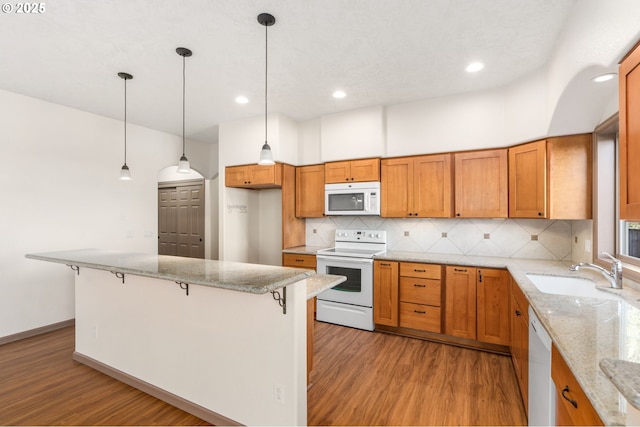 kitchen with a breakfast bar, white appliances, sink, decorative light fixtures, and light stone counters