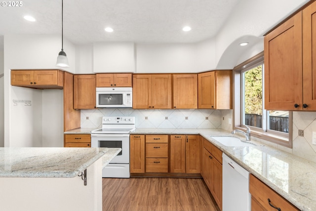 kitchen with light stone countertops, sink, hanging light fixtures, white appliances, and light wood-type flooring