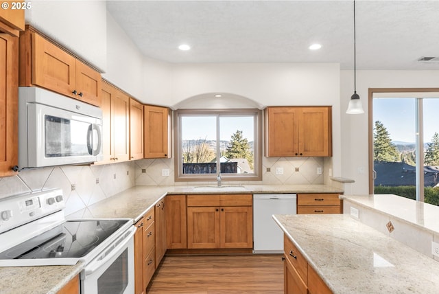 kitchen with pendant lighting, white appliances, backsplash, sink, and light hardwood / wood-style flooring