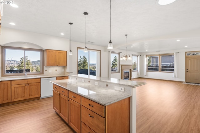 kitchen featuring white dishwasher, decorative light fixtures, light stone counters, and sink