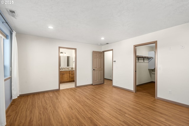 unfurnished bedroom featuring connected bathroom, a spacious closet, light hardwood / wood-style flooring, a textured ceiling, and a closet