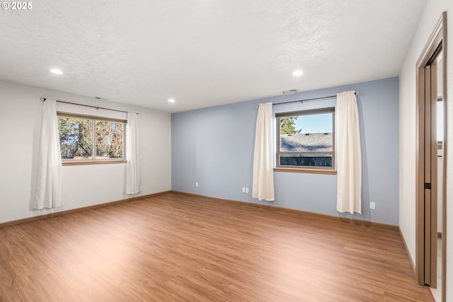 unfurnished room featuring plenty of natural light, a textured ceiling, and light hardwood / wood-style flooring