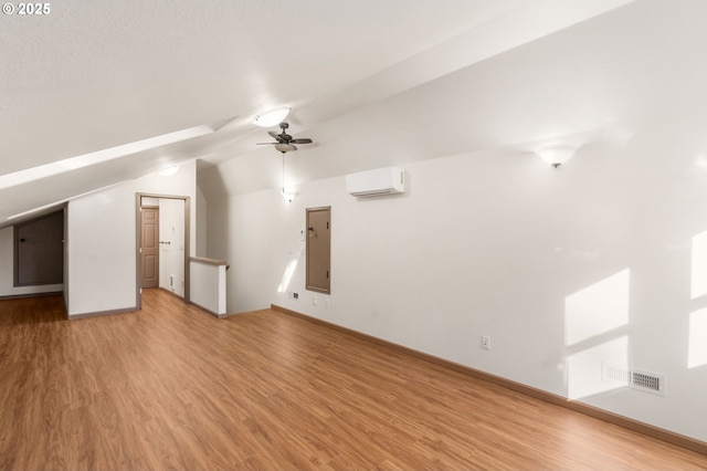 additional living space featuring an AC wall unit, ceiling fan, vaulted ceiling, and light wood-type flooring