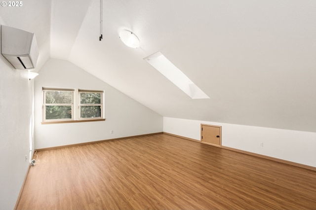 additional living space with wood-type flooring, an AC wall unit, and lofted ceiling with skylight