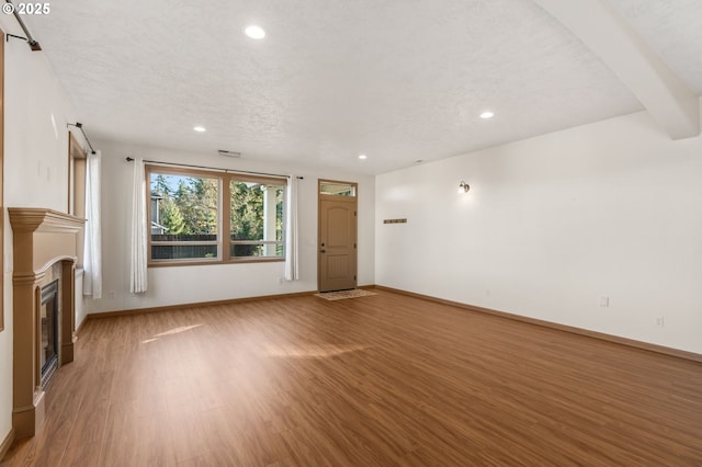 unfurnished living room featuring wood-type flooring, a textured ceiling, and beam ceiling