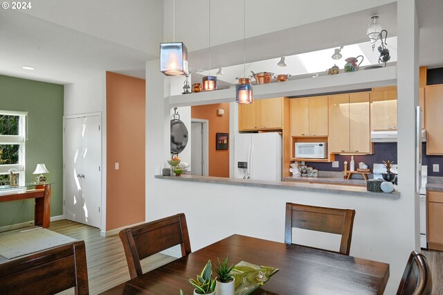 kitchen featuring white appliances, dark wood-style flooring, under cabinet range hood, light brown cabinets, and pendant lighting