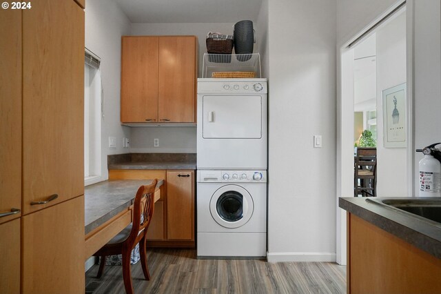 laundry area featuring baseboards, dark wood-type flooring, cabinet space, and stacked washer / drying machine