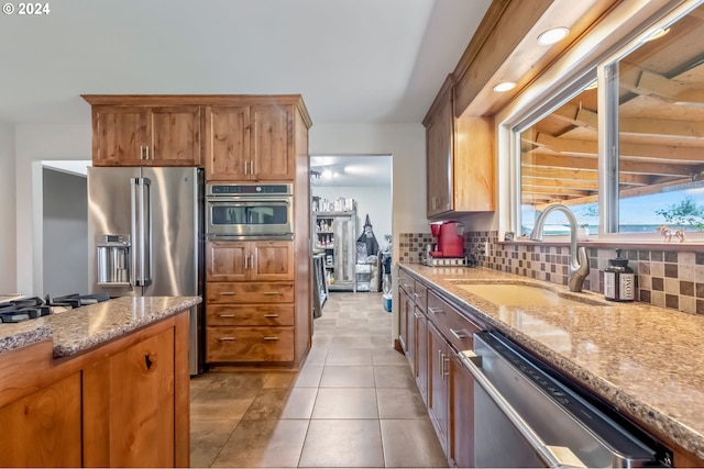 kitchen with stainless steel appliances, decorative backsplash, sink, light stone counters, and light tile patterned floors