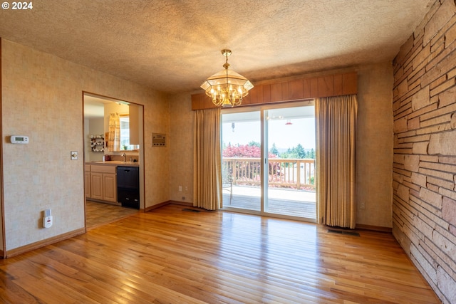 empty room with sink, a textured ceiling, light wood-type flooring, and a chandelier