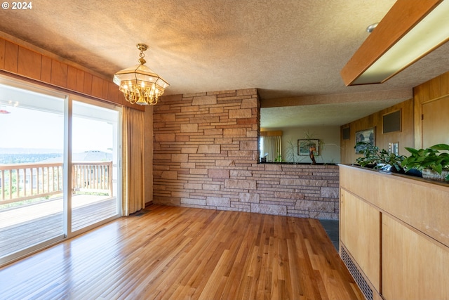 unfurnished dining area with an inviting chandelier, wood walls, light wood-type flooring, and a textured ceiling