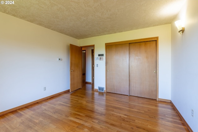 unfurnished bedroom featuring a textured ceiling, a closet, and wood-type flooring