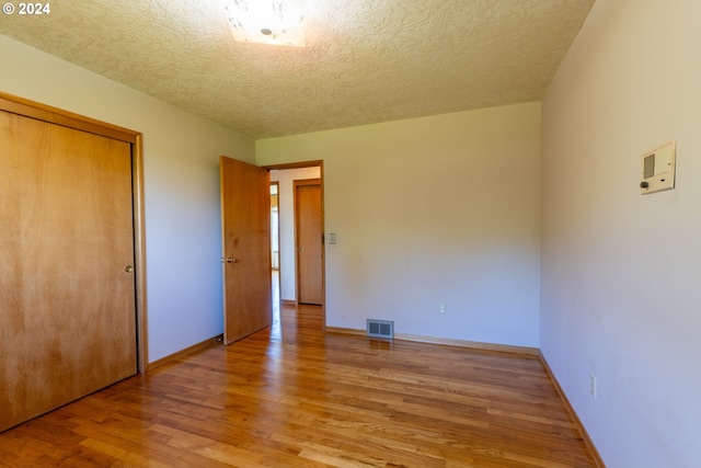 unfurnished bedroom featuring a textured ceiling, a closet, and wood-type flooring