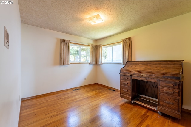 unfurnished office featuring light hardwood / wood-style floors and a textured ceiling