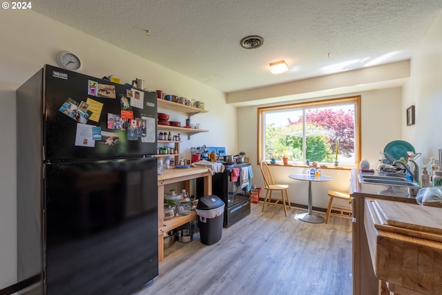 kitchen featuring sink, light wood-type flooring, black appliances, and a textured ceiling