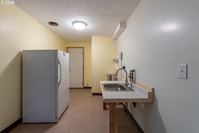 kitchen with sink, a textured ceiling, white refrigerator, and light tile patterned floors