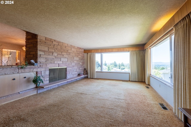 unfurnished living room with a textured ceiling, a stone fireplace, a wealth of natural light, and light colored carpet