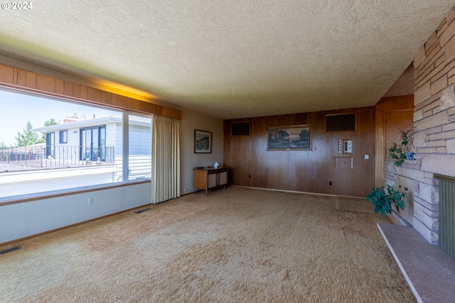 unfurnished living room with a fireplace, carpet, wooden walls, and a textured ceiling