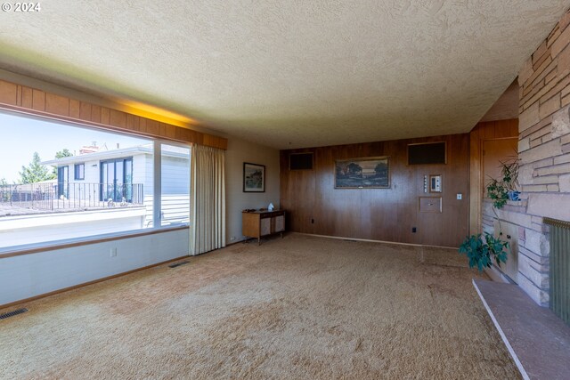 unfurnished living room featuring carpet, a textured ceiling, a fireplace, and wood walls