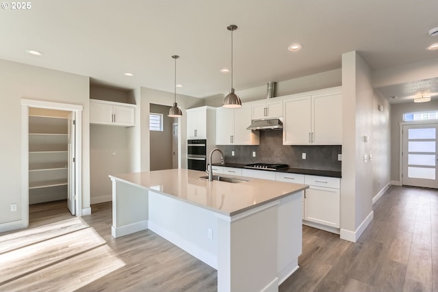 kitchen with sink, white cabinets, hanging light fixtures, gas cooktop, and a kitchen island with sink