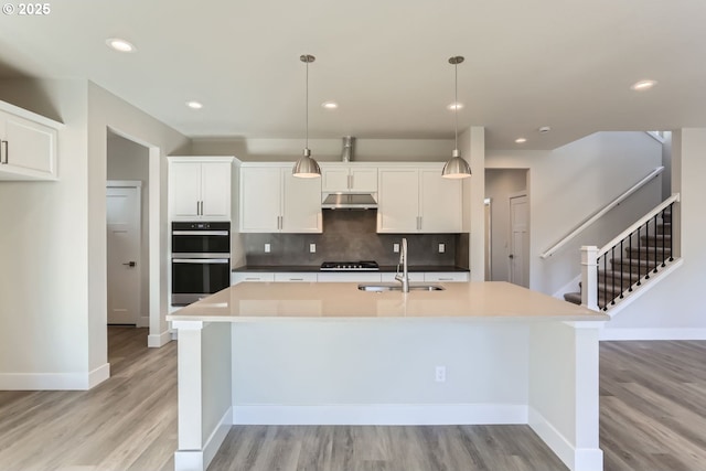 kitchen featuring sink, white cabinets, stainless steel double oven, and decorative light fixtures