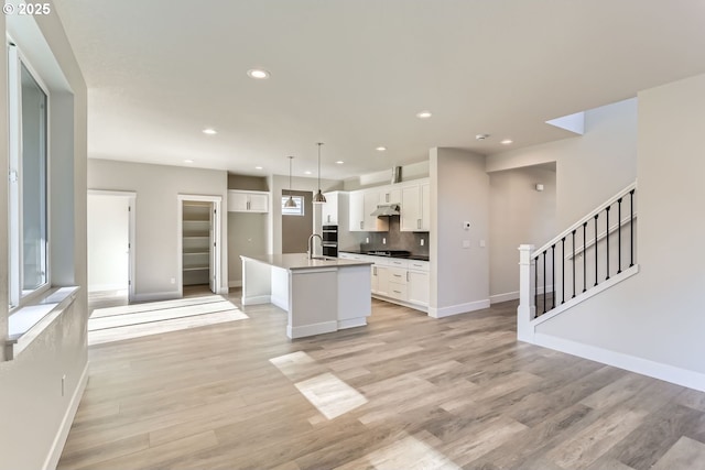 kitchen featuring an island with sink, light hardwood / wood-style flooring, decorative light fixtures, backsplash, and white cabinets