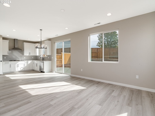 unfurnished living room with light wood-type flooring, an inviting chandelier, a wealth of natural light, and sink