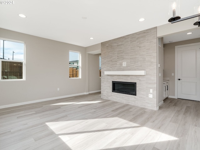 unfurnished living room featuring a tiled fireplace, plenty of natural light, and light hardwood / wood-style floors