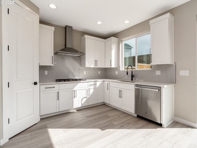 kitchen featuring sink, wall chimney exhaust hood, light hardwood / wood-style flooring, white cabinets, and appliances with stainless steel finishes