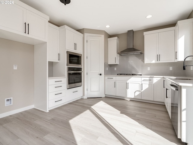 kitchen with white cabinetry, wall chimney range hood, appliances with stainless steel finishes, and light hardwood / wood-style flooring