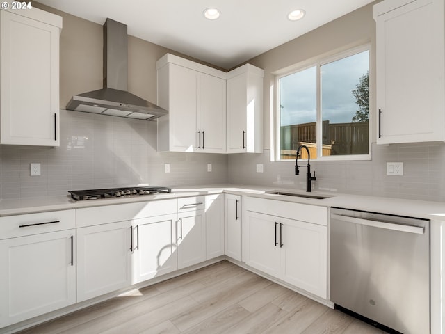 kitchen featuring white cabinets, sink, stainless steel appliances, and wall chimney range hood