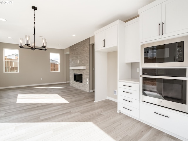 kitchen with black microwave, white cabinetry, oven, a fireplace, and light wood-type flooring