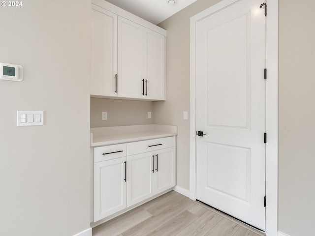 bar with light hardwood / wood-style floors and white cabinetry