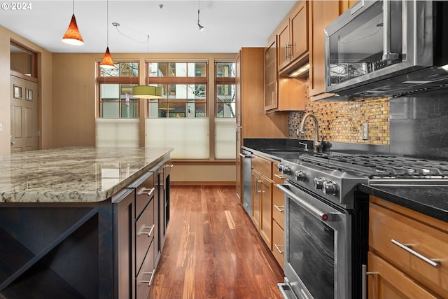 kitchen with pendant lighting, dark stone counters, sink, appliances with stainless steel finishes, and dark hardwood / wood-style flooring