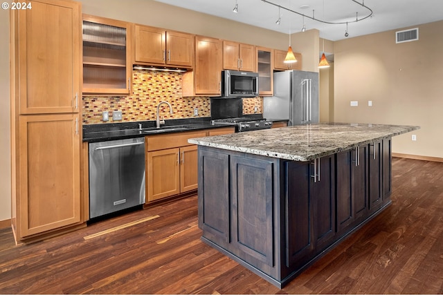 kitchen with sink, a center island, stainless steel appliances, dark wood-type flooring, and dark stone countertops