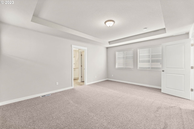 unfurnished bedroom with a textured ceiling, light carpet, connected bathroom, and a tray ceiling