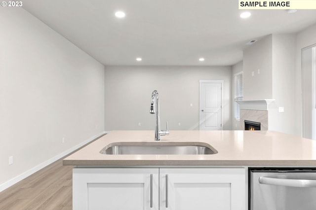 kitchen with dishwasher, white cabinets, a center island with sink, sink, and a fireplace