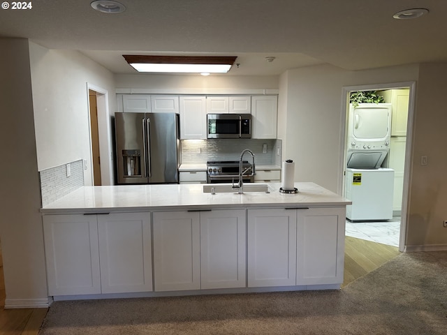 kitchen with sink, white cabinetry, stainless steel appliances, stacked washer / dryer, and decorative backsplash