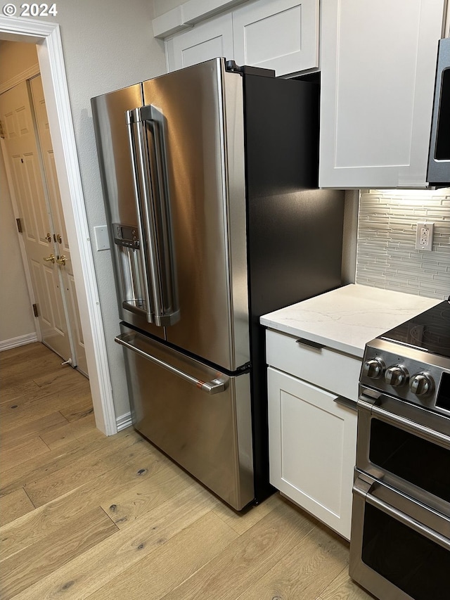 kitchen with decorative backsplash, light stone counters, appliances with stainless steel finishes, white cabinets, and light wood-type flooring