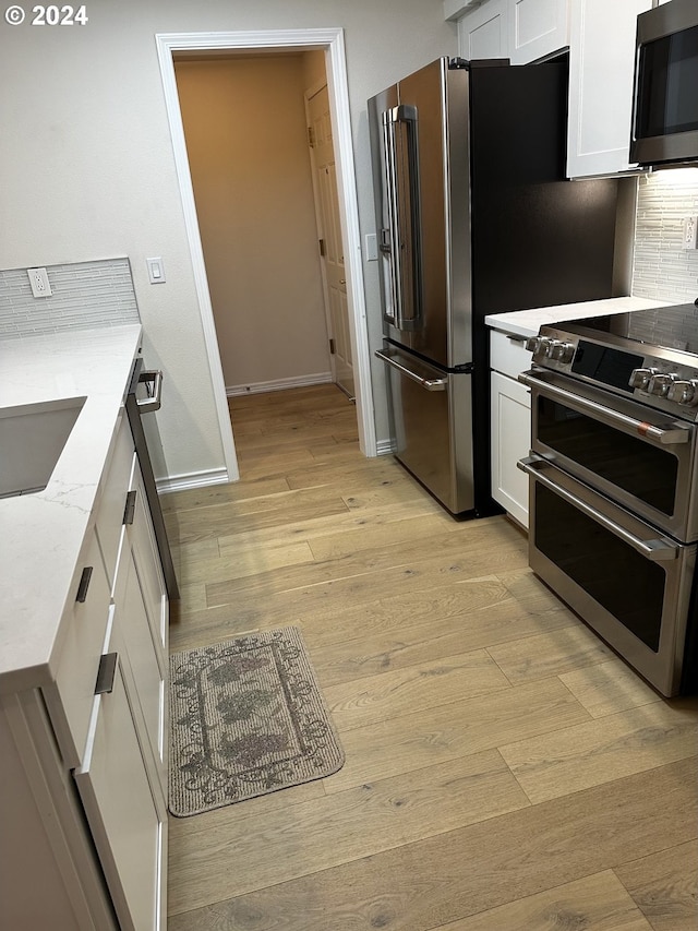 kitchen featuring stainless steel appliances, white cabinets, light stone countertops, light wood-type flooring, and tasteful backsplash