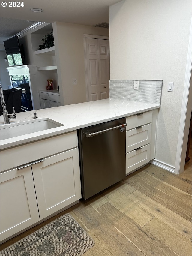 kitchen with sink, white cabinetry, stainless steel dishwasher, light hardwood / wood-style flooring, and light stone counters