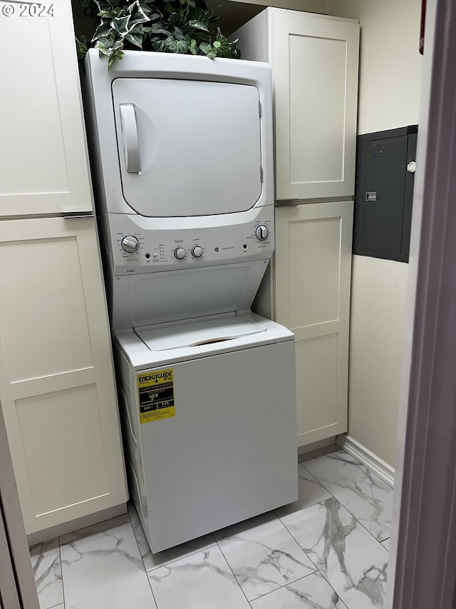 clothes washing area with light tile patterned floors, cabinets, electric panel, and stacked washer / dryer