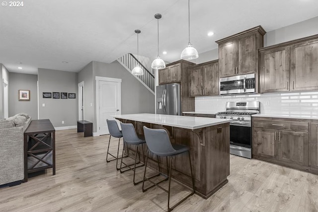 kitchen featuring a breakfast bar, stainless steel appliances, decorative light fixtures, light hardwood / wood-style floors, and a kitchen island