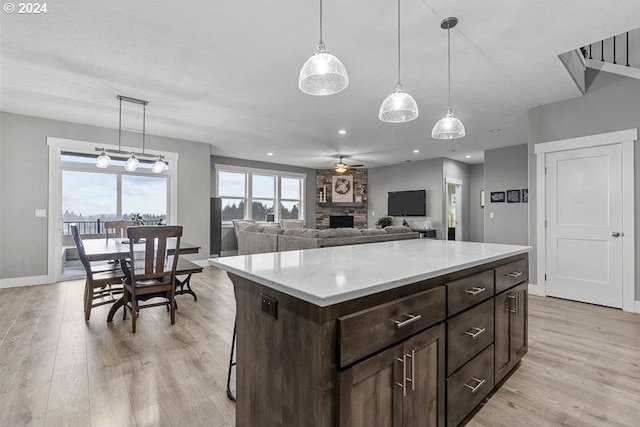 kitchen featuring a stone fireplace, a kitchen island, light hardwood / wood-style floors, and decorative light fixtures