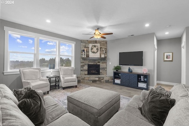 living room with light wood-type flooring, a stone fireplace, and ceiling fan