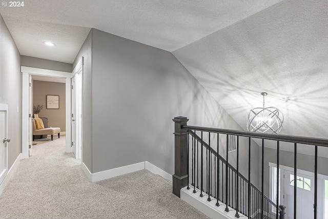 corridor featuring vaulted ceiling, carpet floors, a textured ceiling, and a notable chandelier