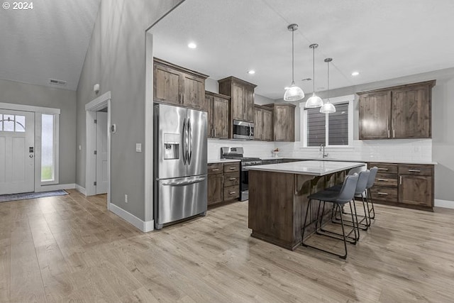 kitchen with appliances with stainless steel finishes, a breakfast bar, decorative light fixtures, light hardwood / wood-style flooring, and a center island