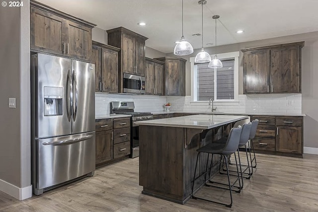 kitchen featuring a kitchen breakfast bar, appliances with stainless steel finishes, decorative light fixtures, a kitchen island, and light wood-type flooring