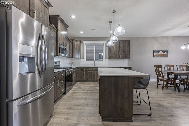 kitchen featuring hanging light fixtures, light hardwood / wood-style flooring, a kitchen island, and stainless steel appliances