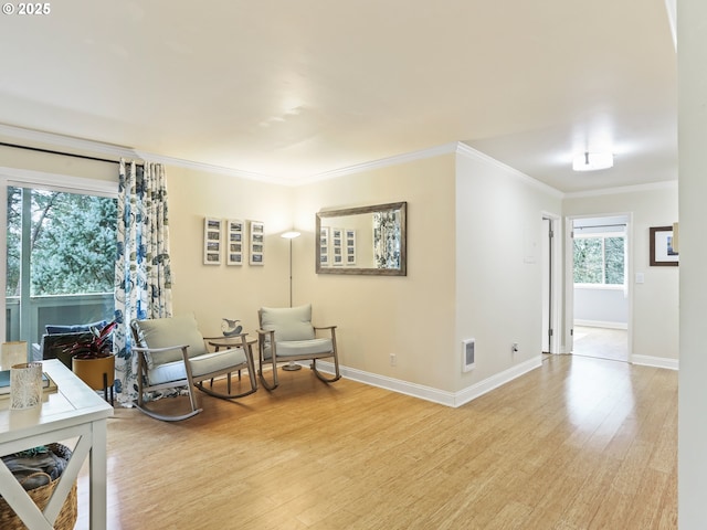 sitting room featuring ornamental molding, light wood-type flooring, visible vents, and baseboards