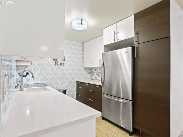 kitchen featuring light wood finished floors, white cabinets, freestanding refrigerator, dark brown cabinets, and a sink